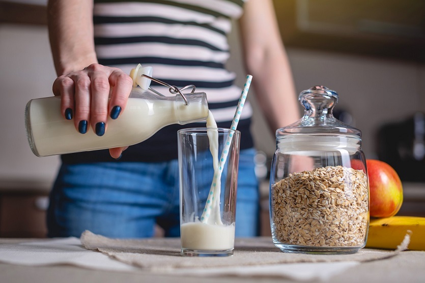 Woman pours Oat Milk from Powder in a Glas